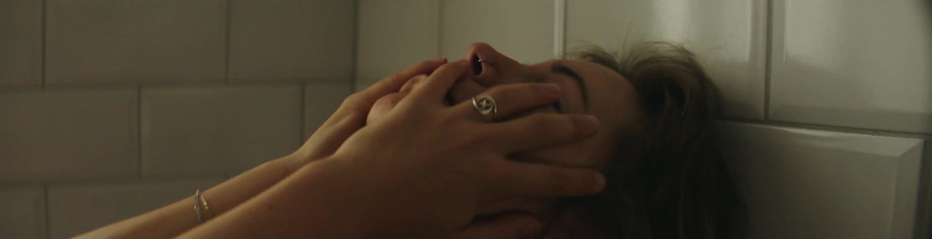 A woman leans her head against a tile wall and moves her hands on her face and chest as she tries to relax