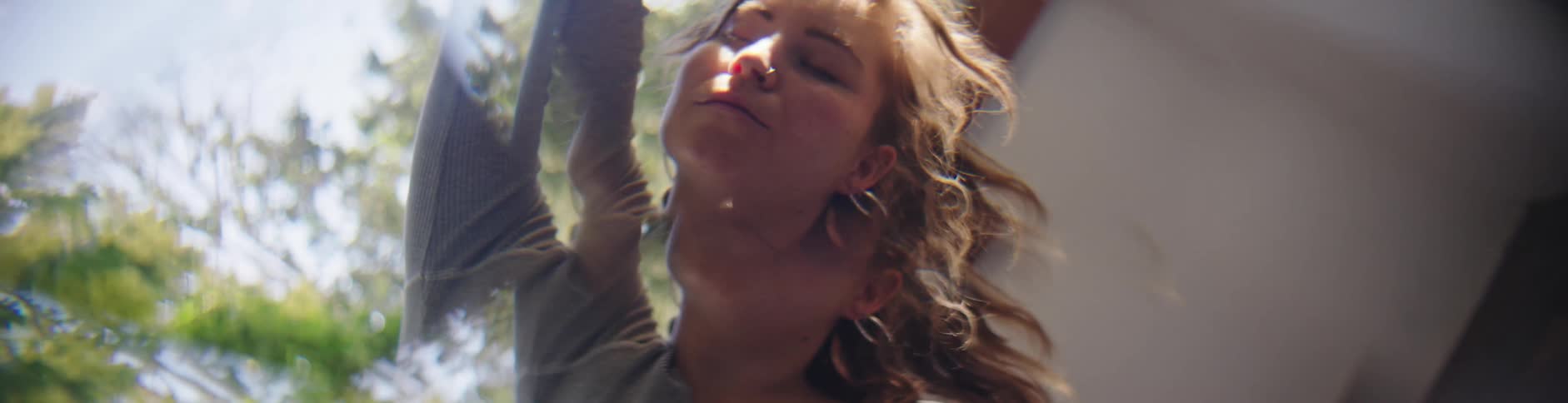 A white woman stretching in her backyard filled with trees