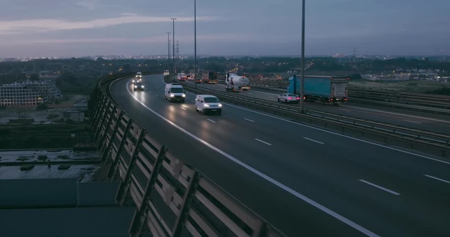 Numerous cars and freight trucks drive along a raised highway