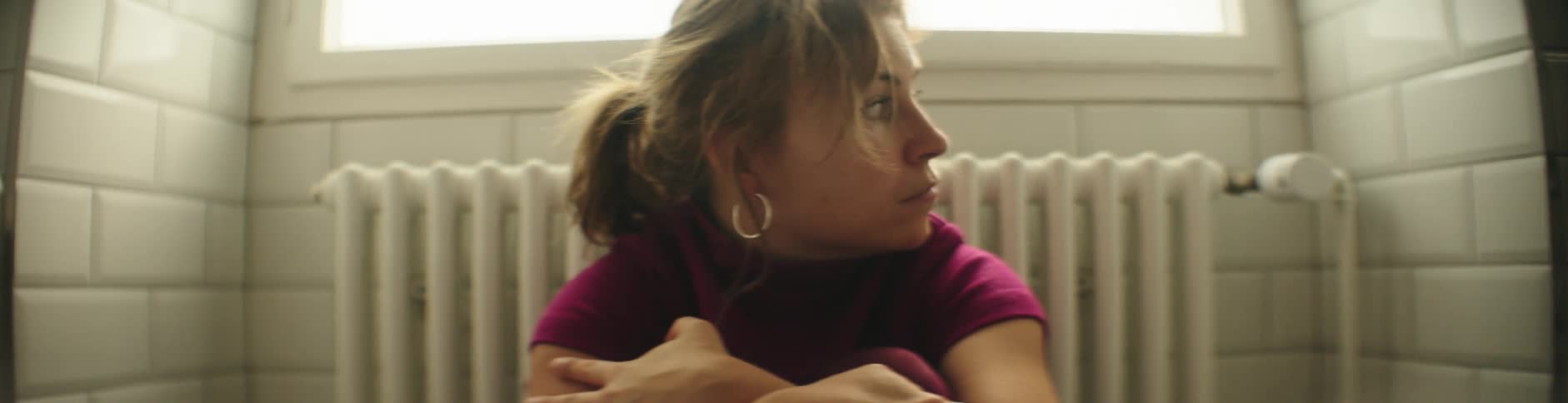 Woman with brown hair hoop earrings and red top looks around in a small room