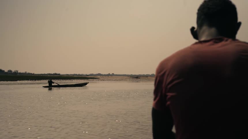 A fisherman sits on a boat wearing a red tshirt his back facing the water as he prepares for a day of fishing