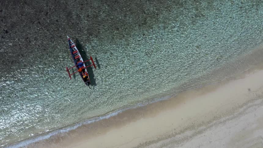 A canoe with two people in it is floating away from the sandy beach