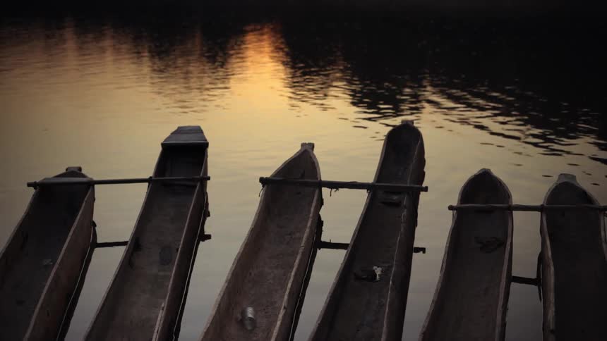 Three double canoes floating by the river bank at sunset