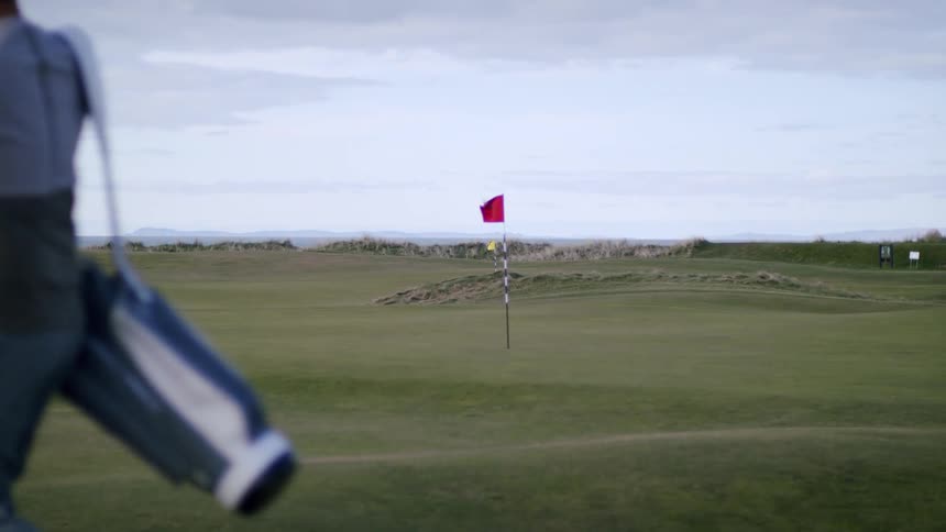 Golfer picks up golf bag and walks away from area near golf hole