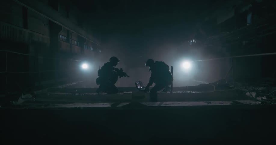 Two soldiers are atop a building as one has his gun ready