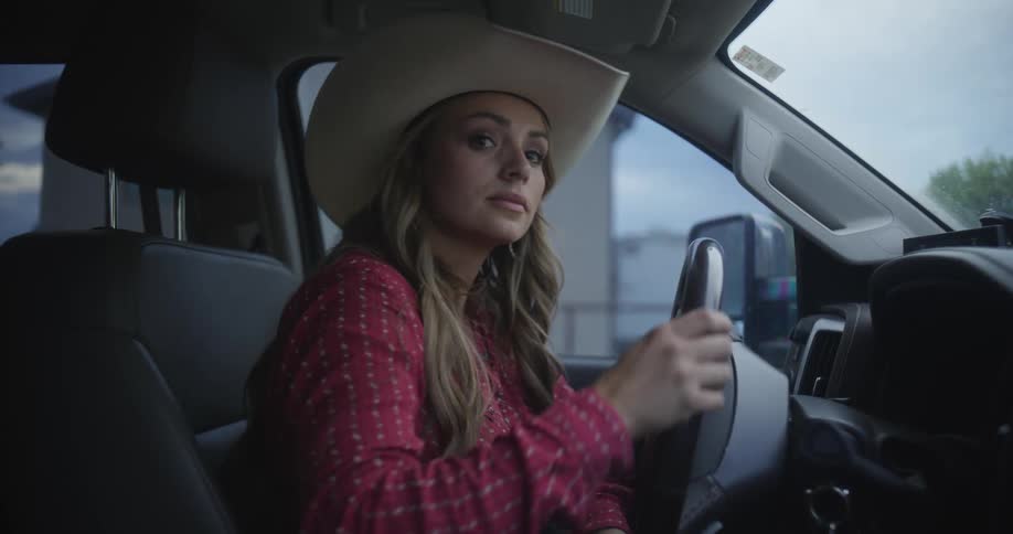 A blondie female with cowboy hat driving a car