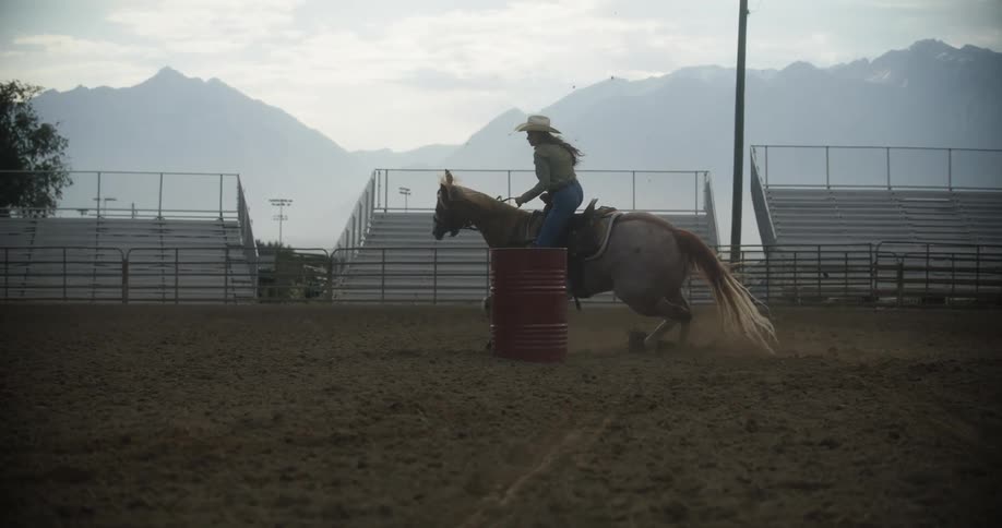 Cowgirl rides a horse around a red barrel in the rodeo