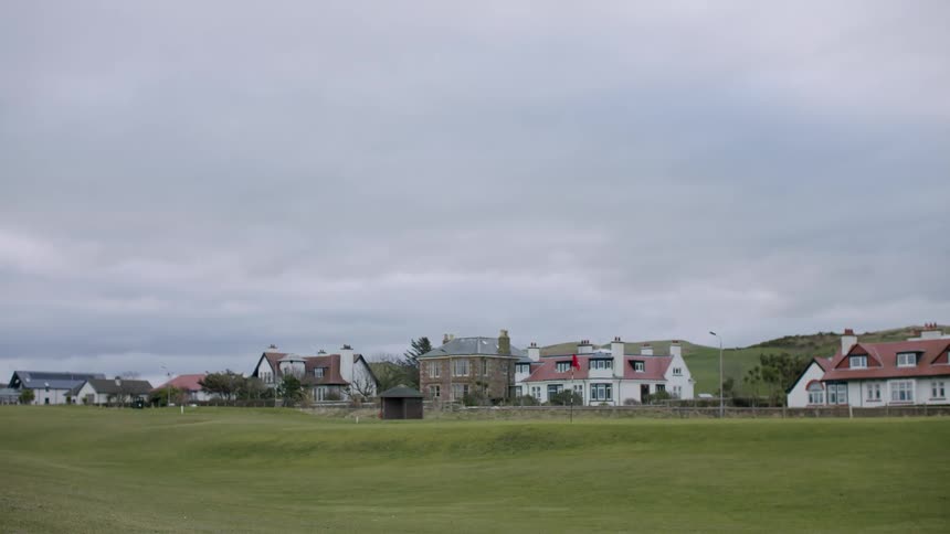 A sub urban area with houses and residential buildings with a large grass land area