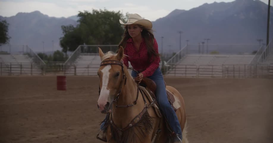 A woman wearing a cowboy hat riding a horse on an empty racetrack