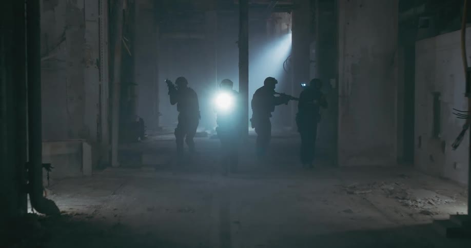 A tactical team of police officers with guns and flashlights are walking prepared on a concrete path