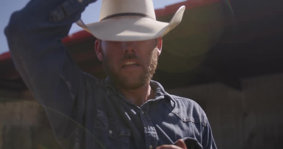 A man with cowboy hat is sweating and puts his sleeves on his forehead
