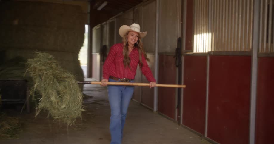 Cowgirl carries hay with a fork into a stable