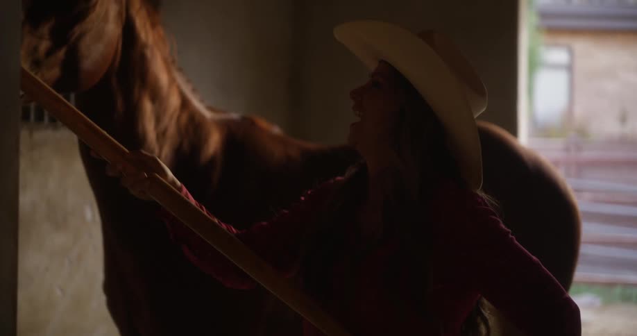 Cowgirl feeds hay to a horse in a stable
