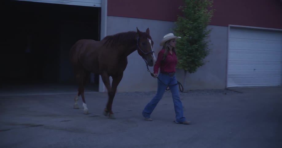 A woman in a cowboy hat leads a horse to a caravan