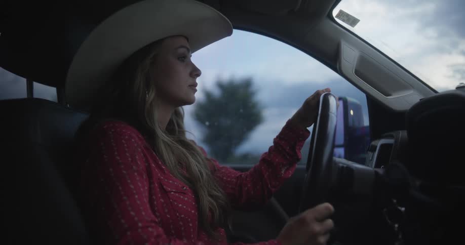 A blonde girl with a hat is driving a car