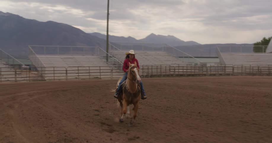 Woman riding her horse fast in an empty rodeo stadium structure