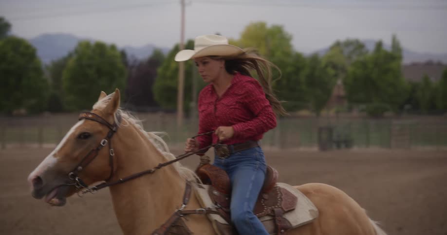 A cowgirl is riding a horse and is wearing a hat