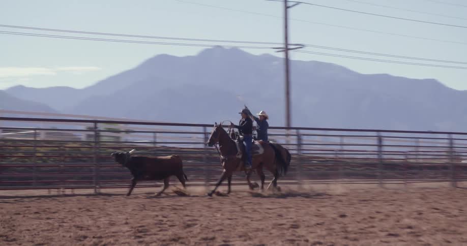 Two people are each riding a horse in a dirt covered enclosure at a ranch