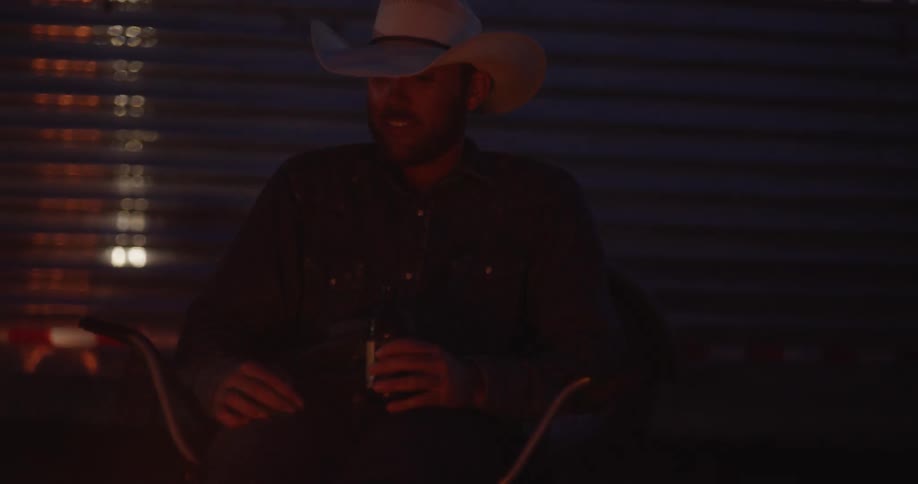 A cowboy drinks a beer by the campfire