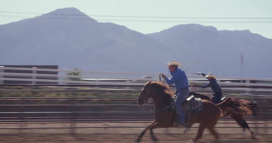 Two cowboys running with horses while rotating ropes