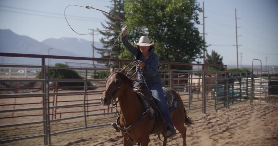 A woman with a hat is riding a horse and spinning a rope