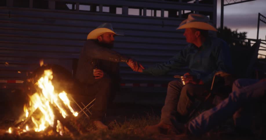 Two cowboys shake hands at the campfire