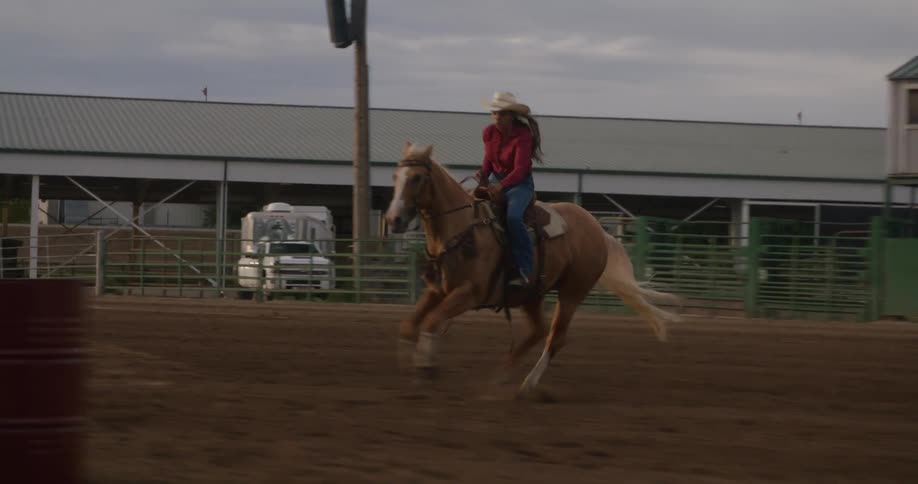 Woman riding a horse at high speed in a rodeo sand arena
