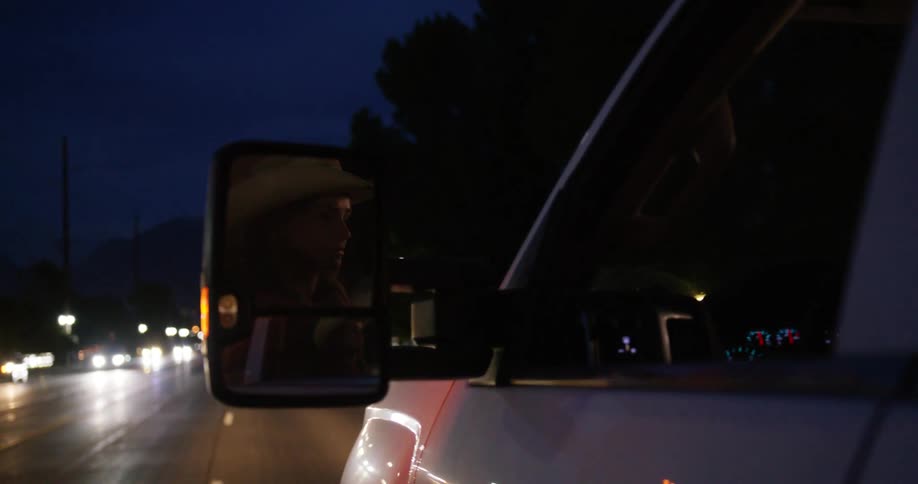 Cowgirl reflecting on the rearview mirror of a moving truck