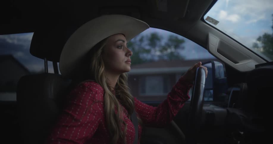 A woman wearing a cowboy hat drives through a residential neighborhood in her truck