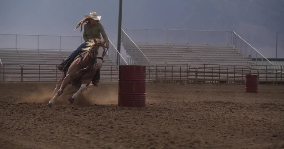Cowgirl rides a horse around a red barrel in the rodeo