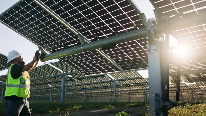 A utility worker holds a hand drill as he works on solar panels