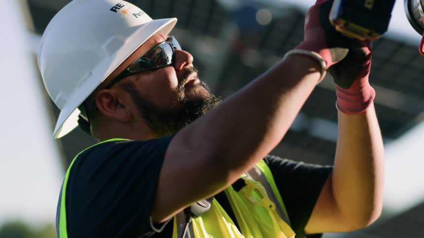 A utility worker is using a drill on solar panels