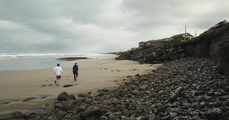 Two people run on a rocky beach