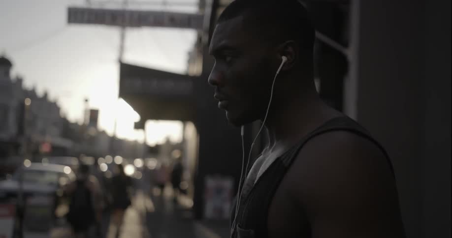 A man stands on a busy sidewalk looking at his phone and around the street