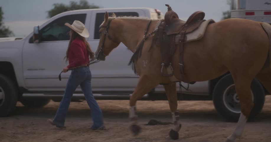 A woman in a cowboy hat walks with a horse on a dirt field
