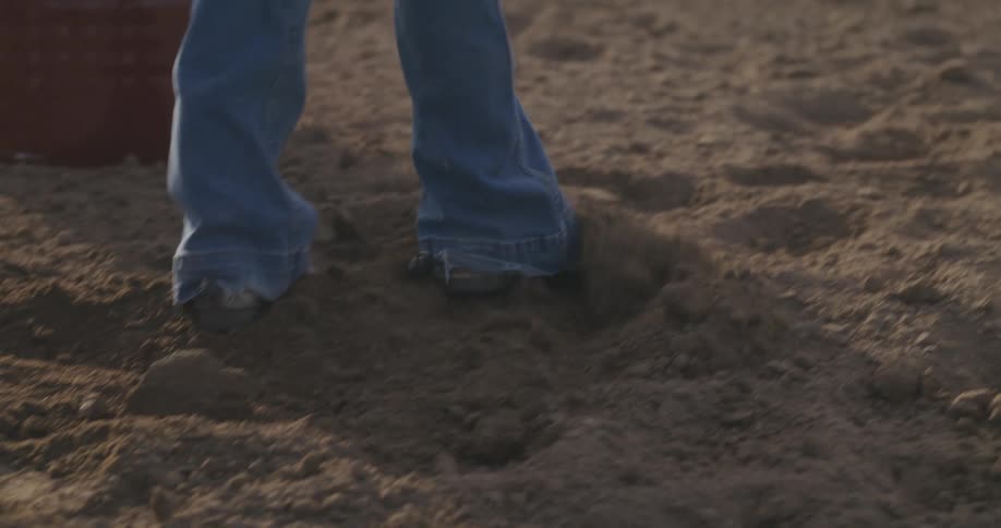 A person using his feet to spread the sand while a horse walks behind them