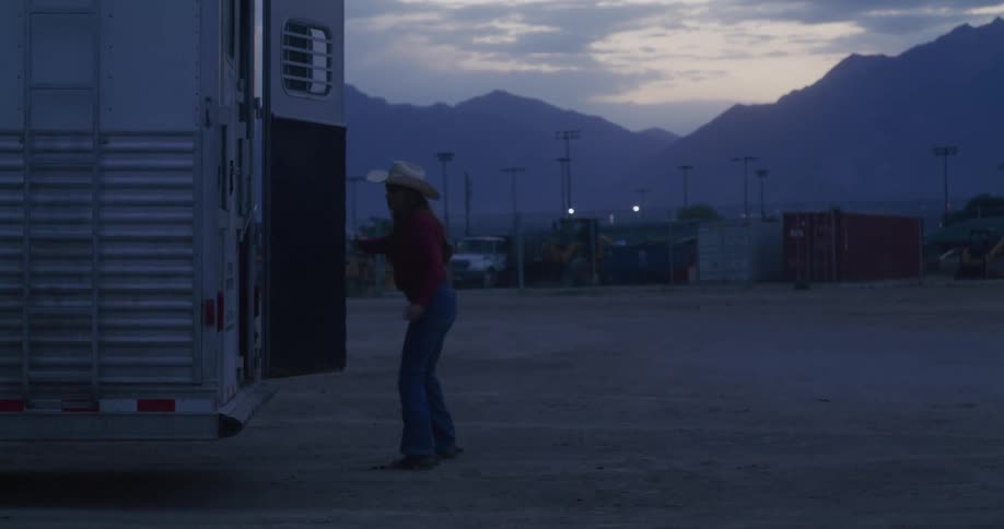Cowgirl loads a horse into a trailer at morning