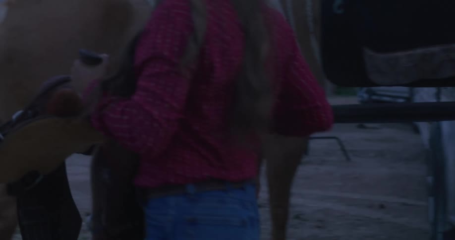A woman in a cowboy hat grabs a saddle and walks to a horse
