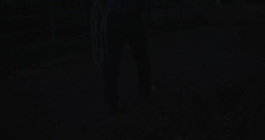 Cowboy walking with his back turned on a ranch under a dark dawn sky