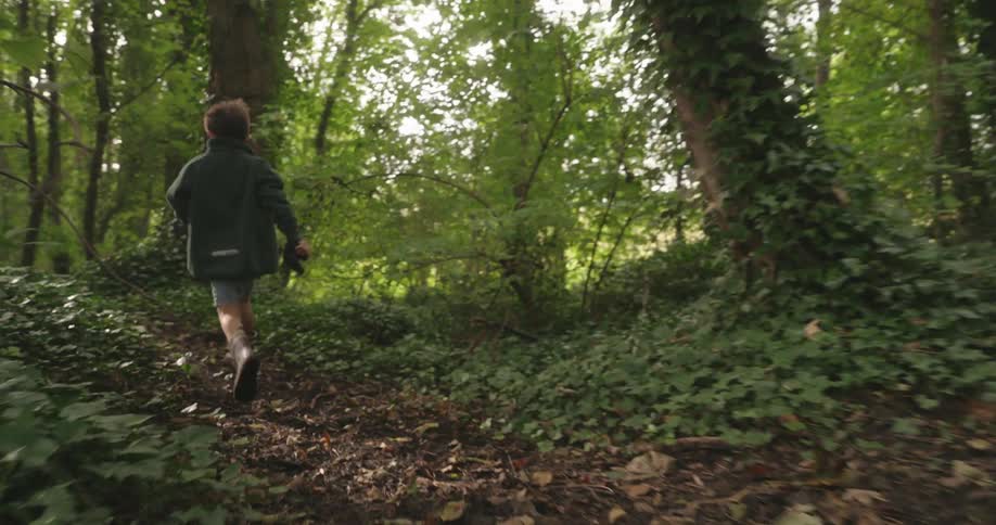 A young boy runs along a forest trail during the daytime