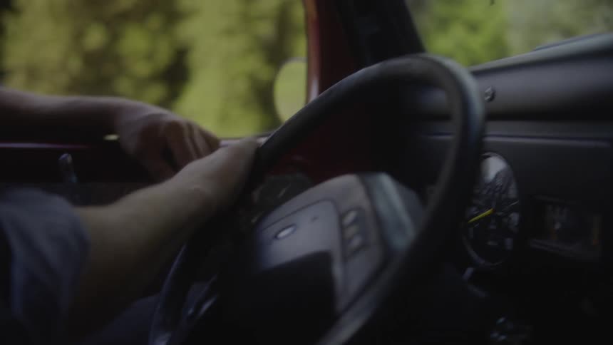 A man turns the steering wheel while driving a car on a sunny day