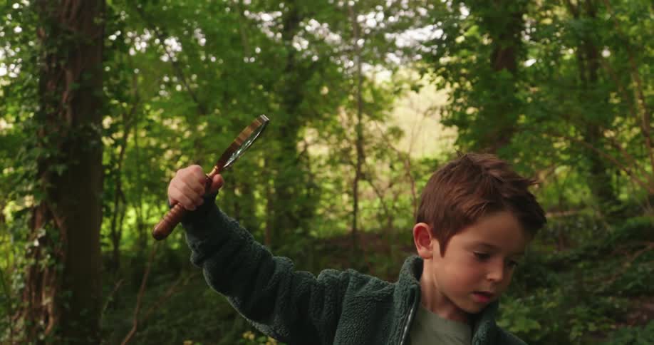 A little boy is standing in the woods holding a magnifying glass
