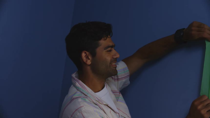 A smiling man is placing a green ribbon next to a window