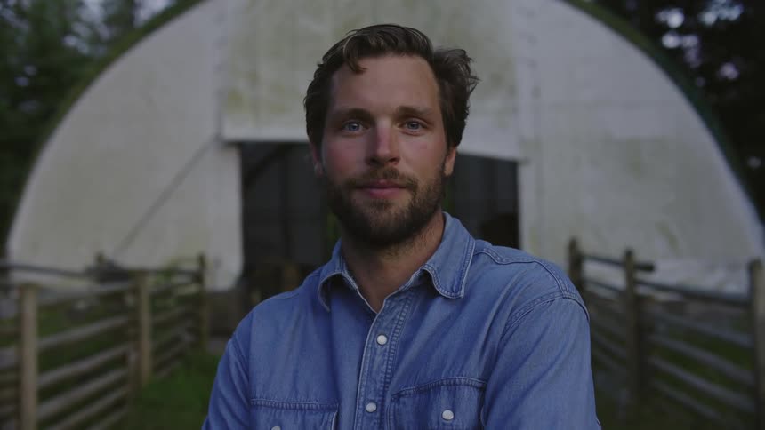 Portrait of a male farmer with crossed arms standing in front of a barn