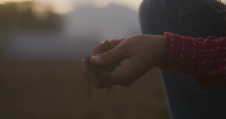 A person picking up sand from the ground
