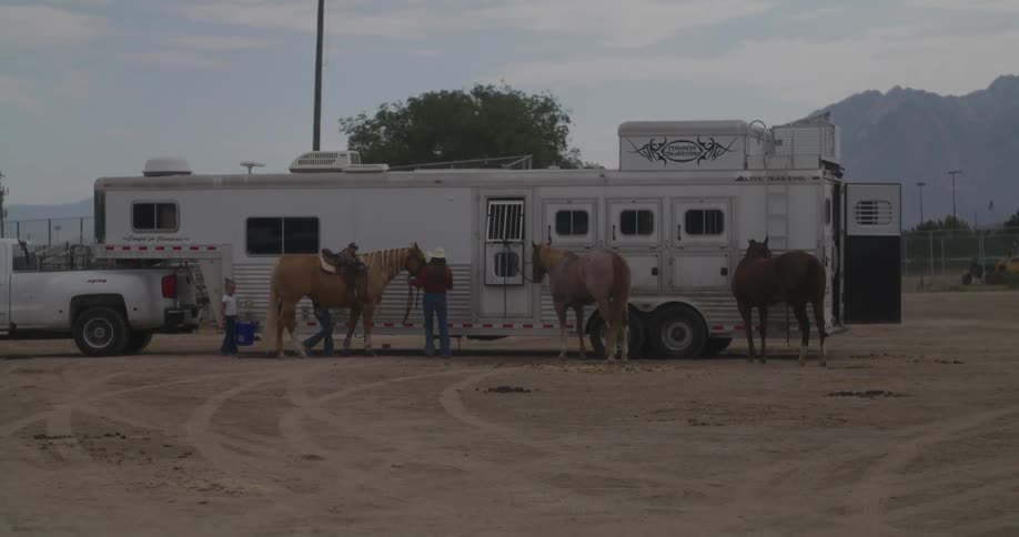 Family and horses stand near horse trailer with mountain in the background
