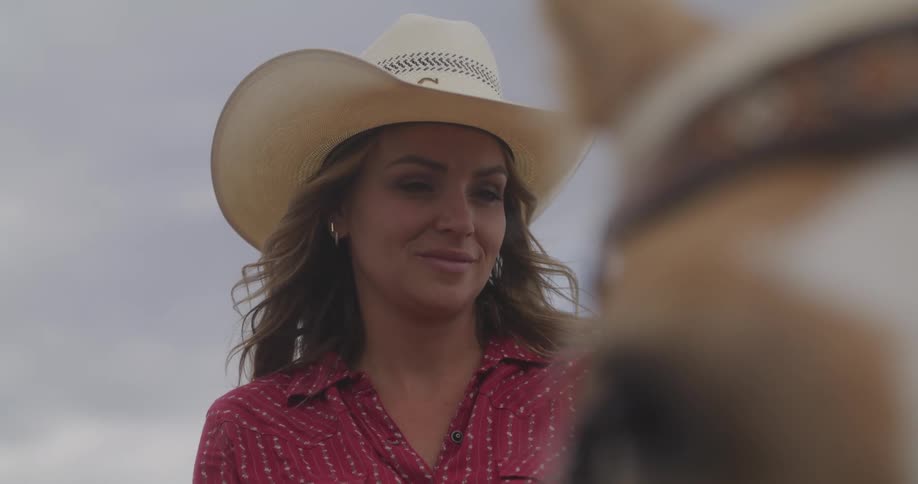 A woman in a cowboy hat is looking at a horse in front of her
