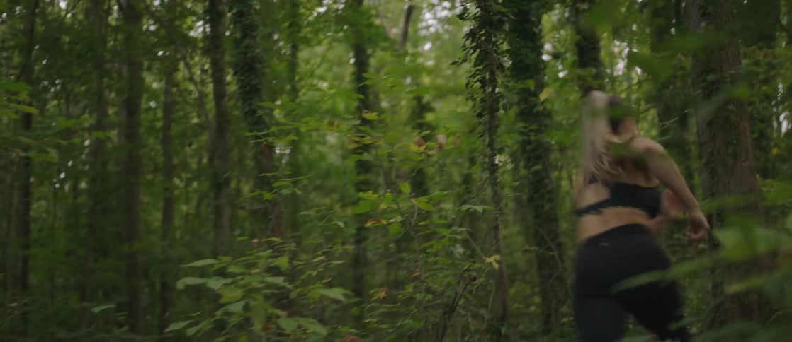 A woman runs fast on a trail in the woods