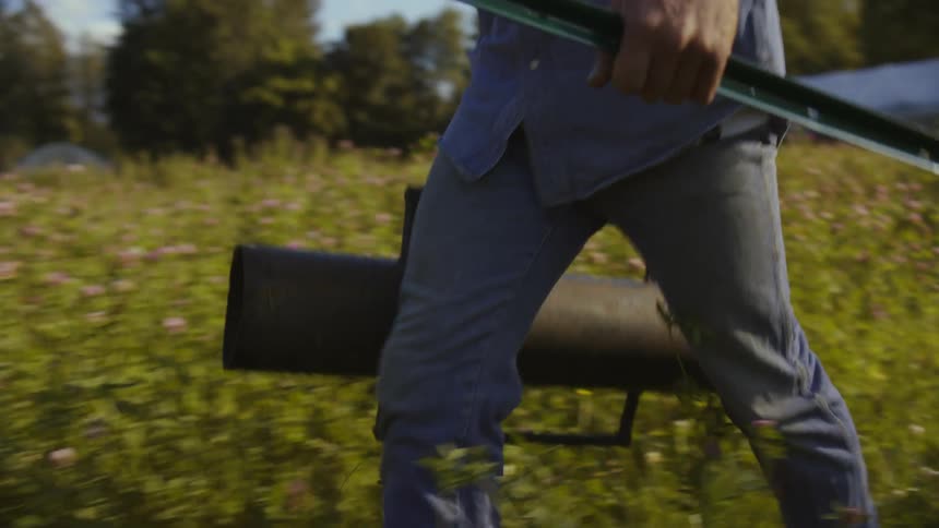Man walking through a farm pasture with work equipment