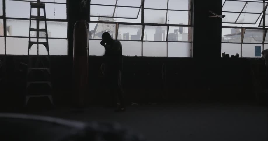 A man walks past windows in a gym and punches a heavy bag